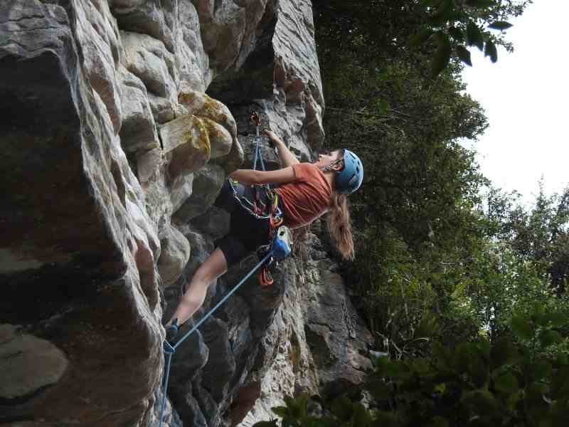 Climber in blue helmet on featured limestone cliff from below